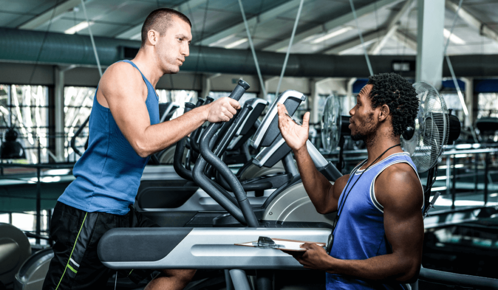 A man coaching his friend running on elliptical