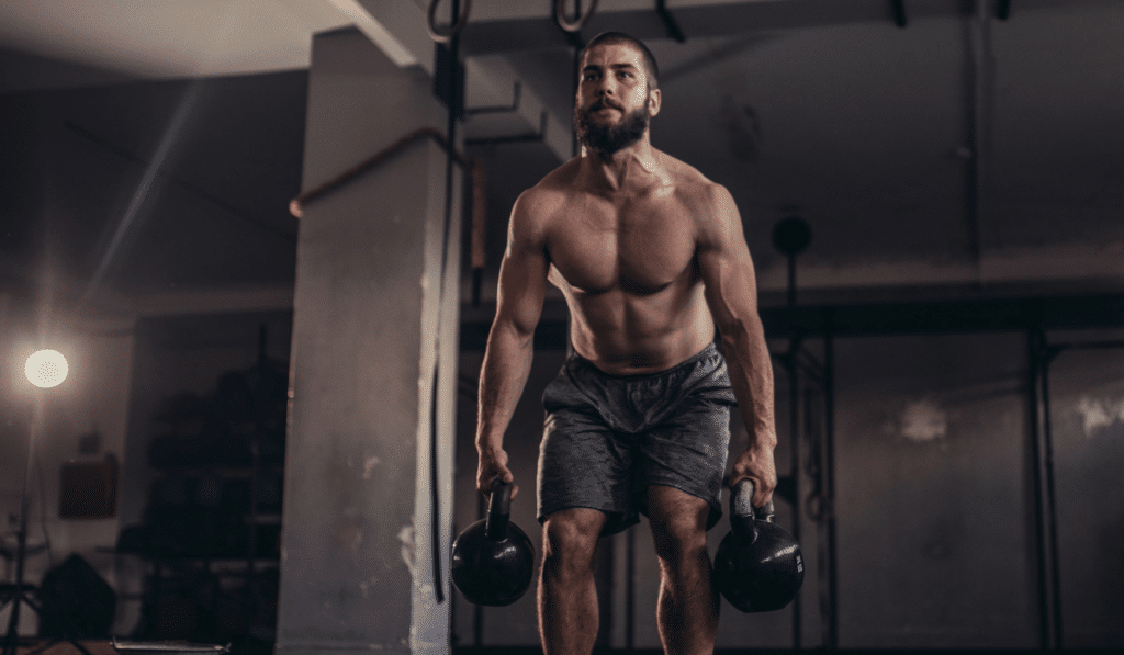 A muscular shirtless man does a deadlift with two kettlebells