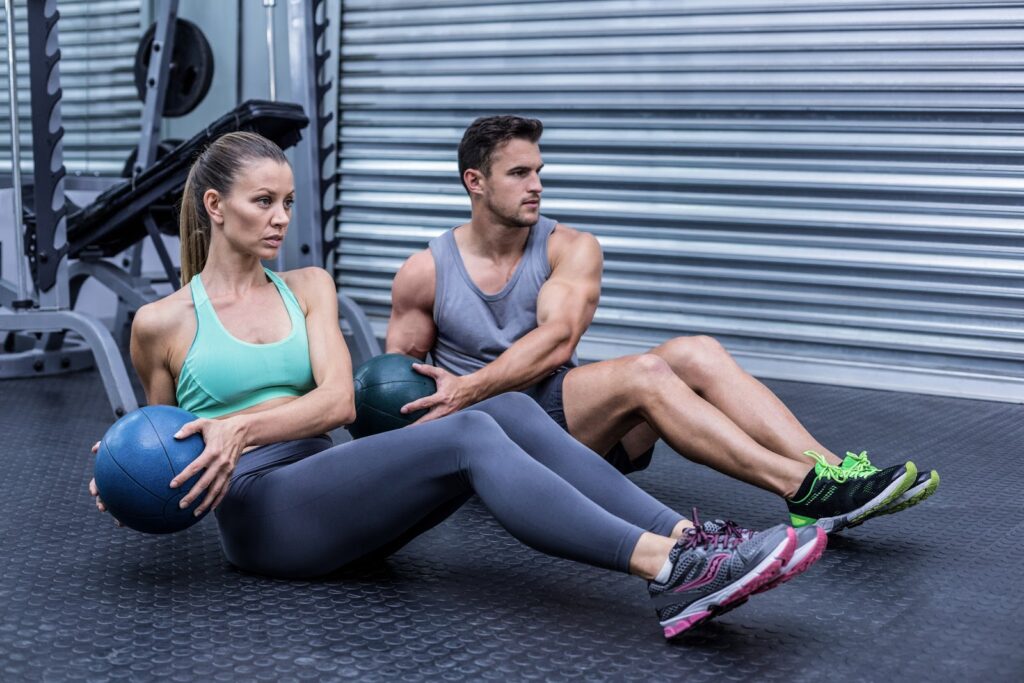 Two people doing russian twists with kettlebells at the gym