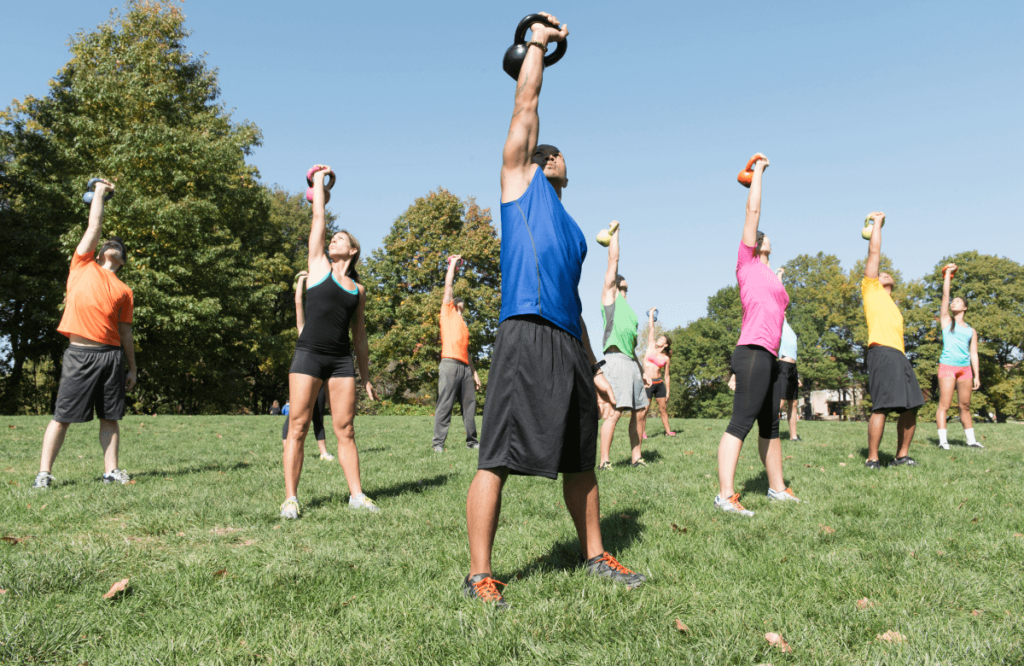 A group of peple doing the kettlebell press exercise outside