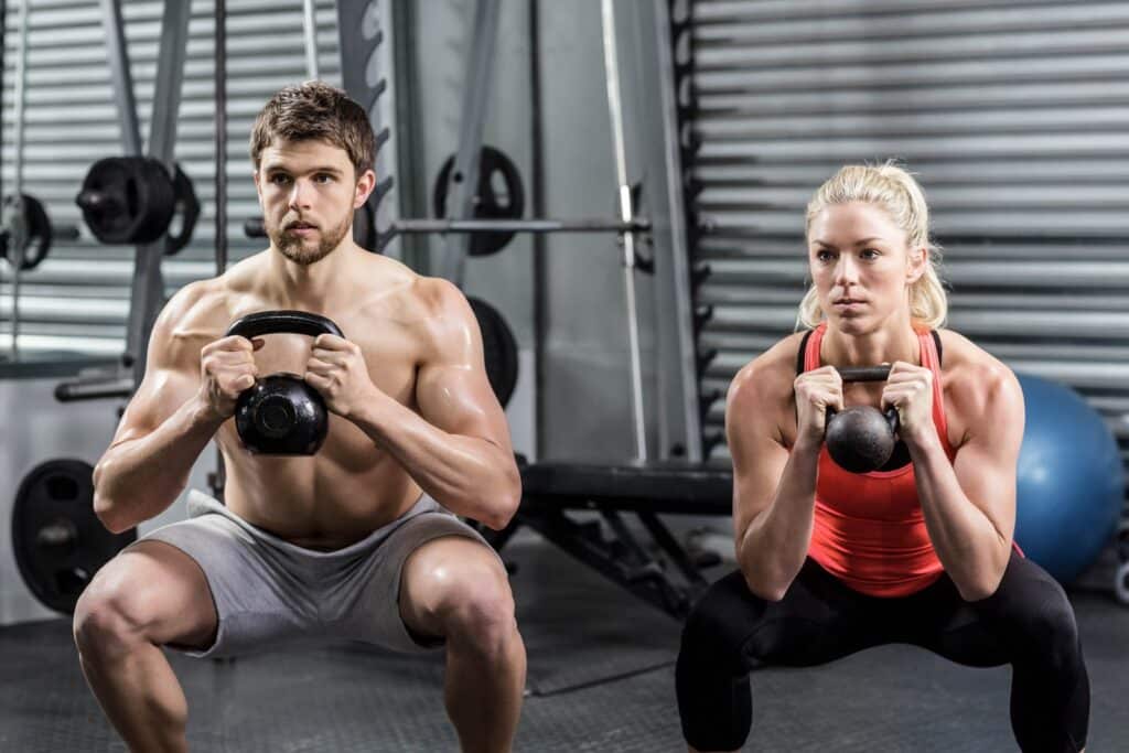 Two athletes at the gym doing the kettlebell thruster exercise