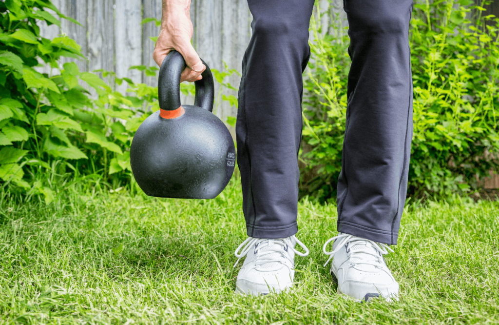 A man doing a kettlebell deadlift in his garden