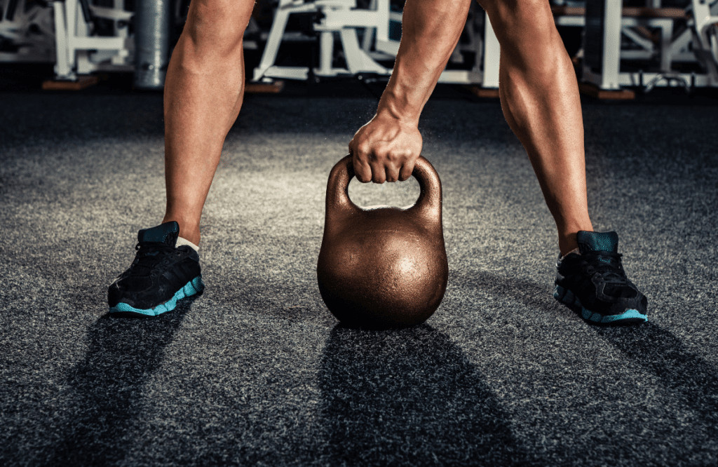 A man at the gym doing kettlebell high pulls showing the muscle worked