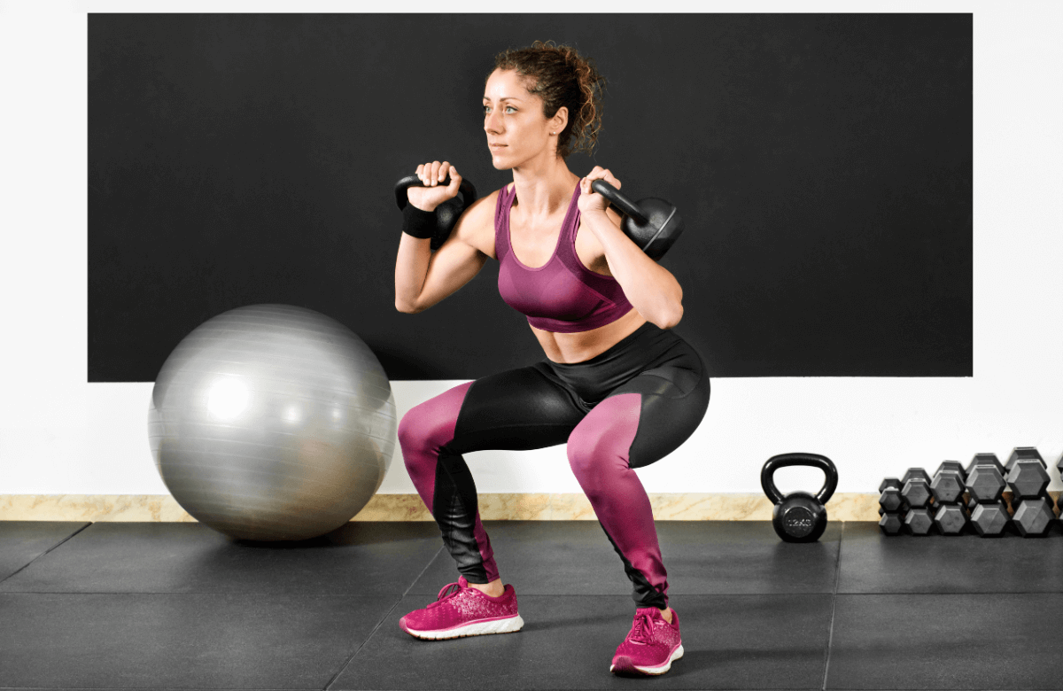 Une femme réalise un front squat avec kettlebells