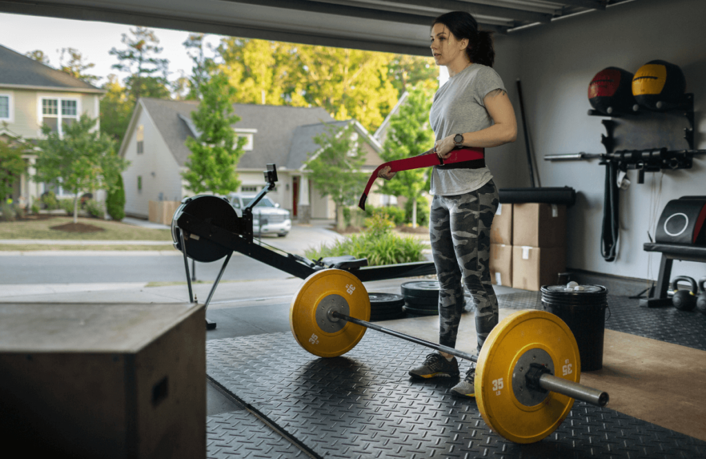 A woman in her home gym tightening her best deadlift belt before lifting