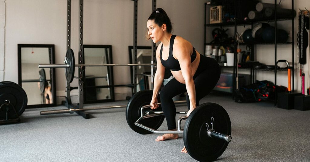 A woman performing deadlifts while pregnant in her garage