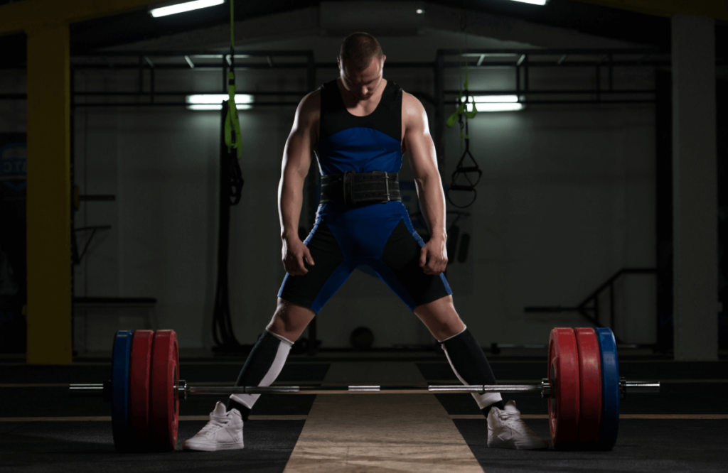 A muscular man about to deadlift wearing a weight lifting belt