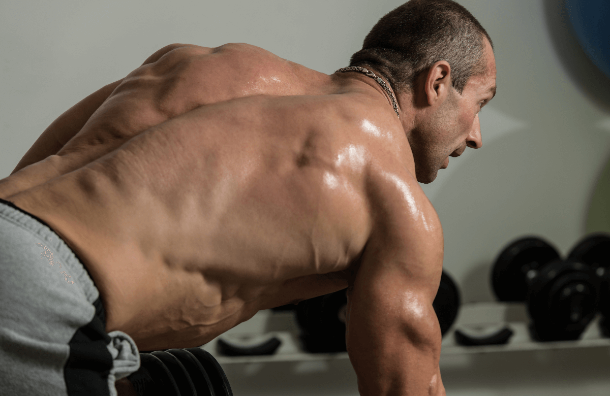A muscular man performing lat workouts with dumbbells
