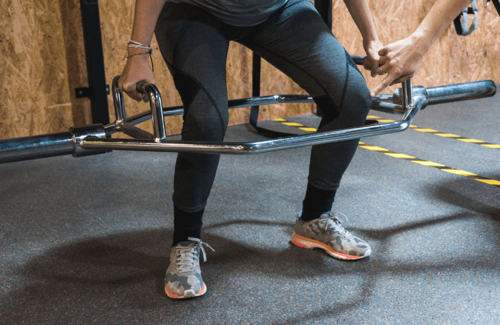 A man performing hex deadlifts with the help of his coach