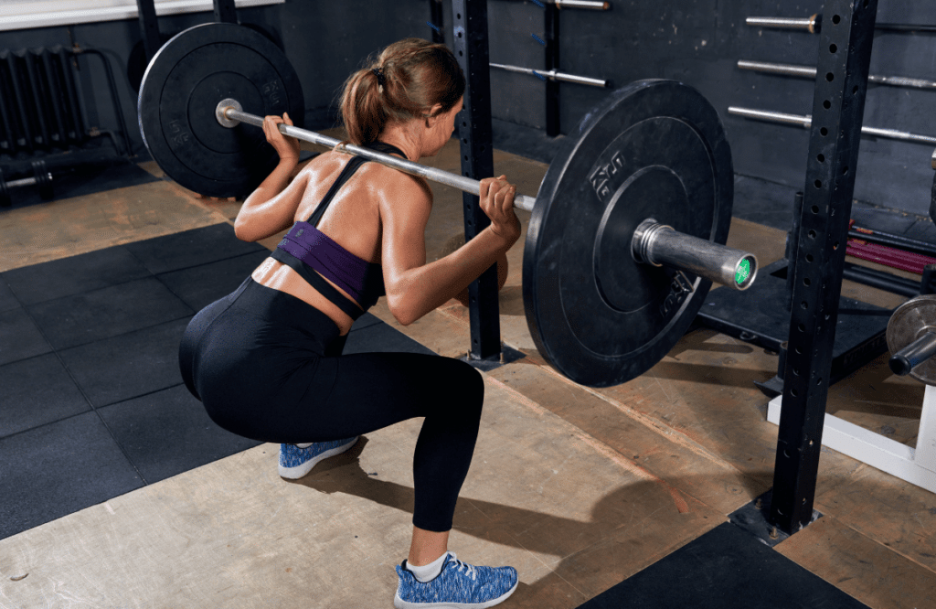A woman doing squats near a rack
