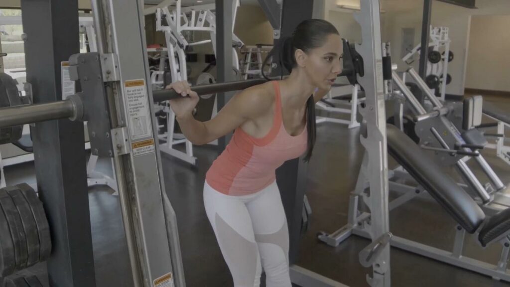 A woman doing smith machine good mornings to strengthen her back