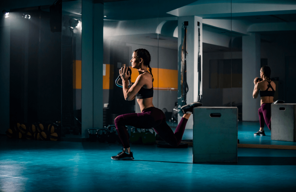 A woman doing bulgarian split squats for glutes at the gym using a box and a kettlebell