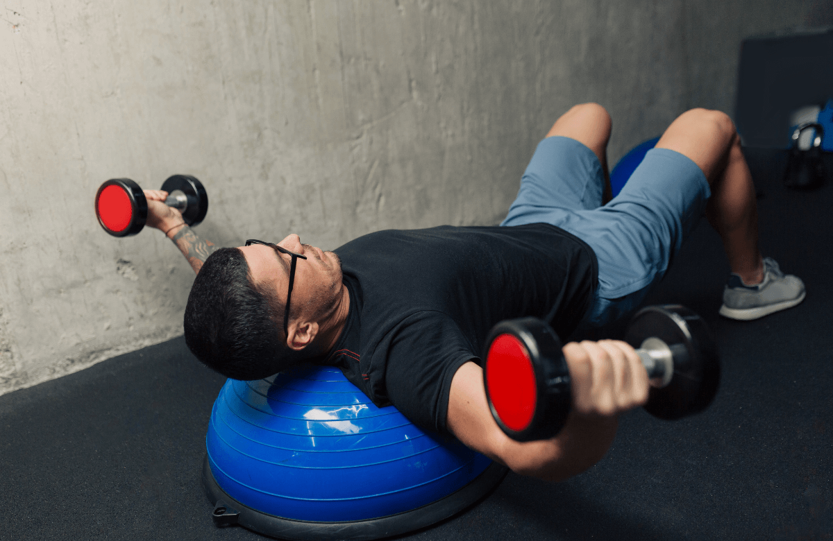 A man performing dumbbell flys on a medicine ball