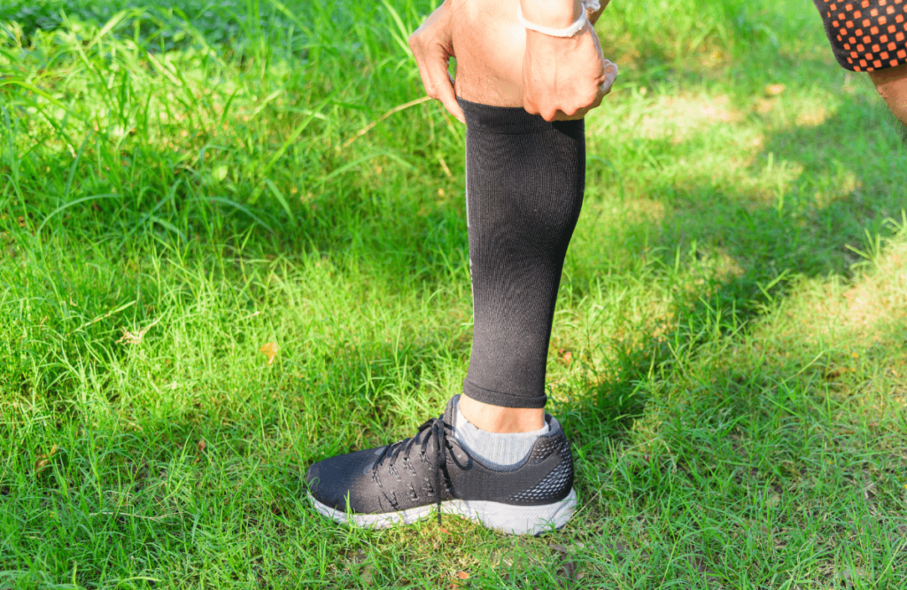 A man in the grass preparing himself with knee sleeves