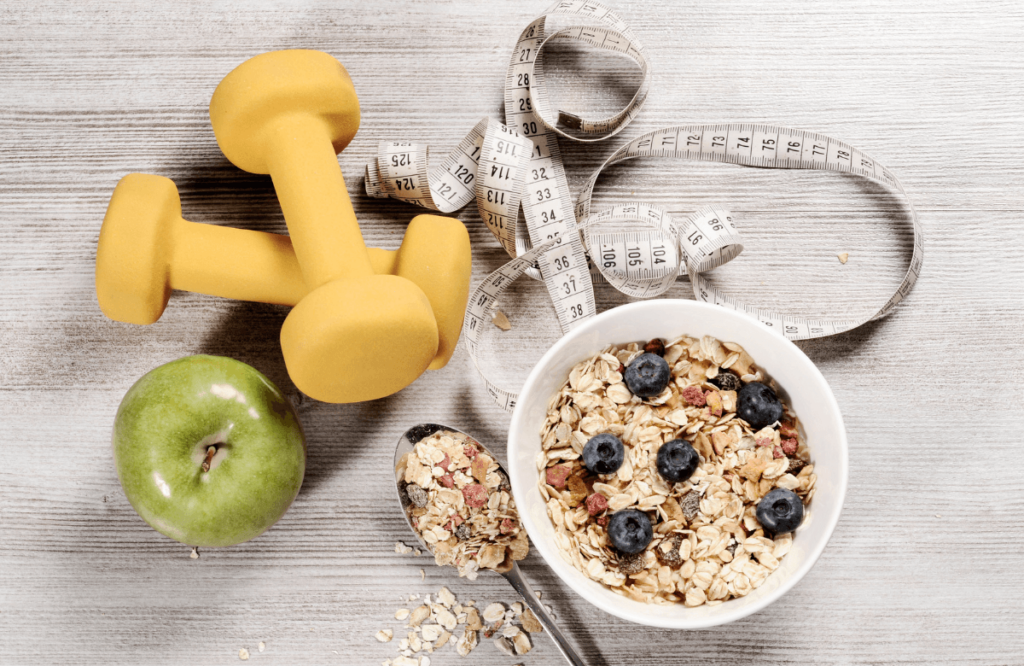 A bowl of oat and berries with an apple near a meter and dumbbells