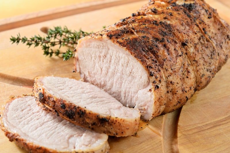 Herb crusted pork tenderloin roast being sliced on a cutting board, warm from the oven.  Thyme garnish.  Very shallow DOF.