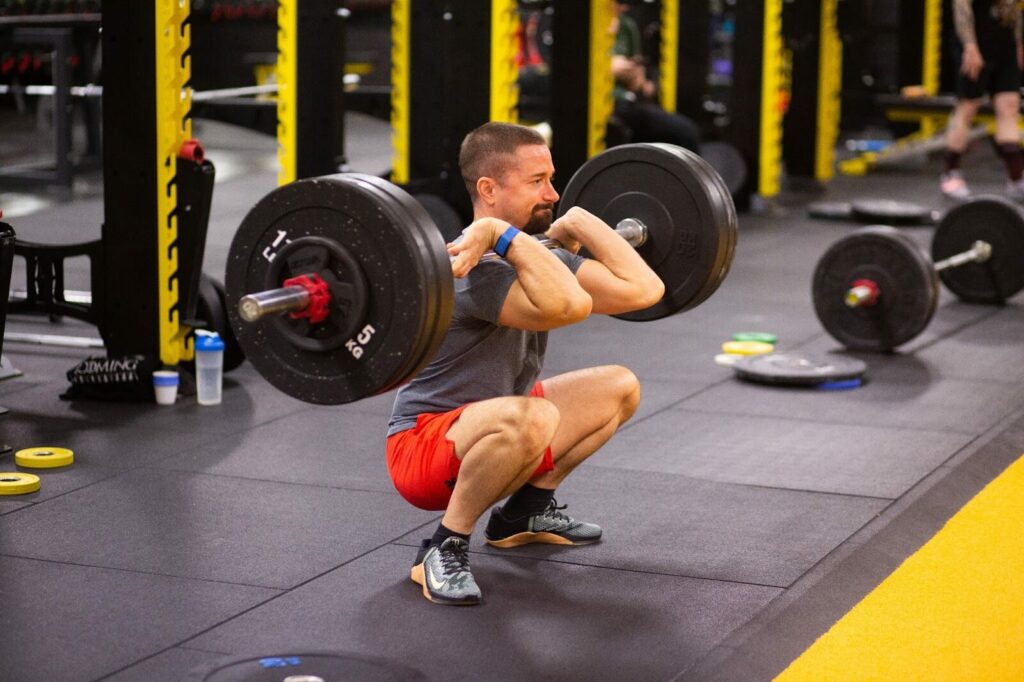 a gorilla is squatting in a gym with a barbell in front of him and