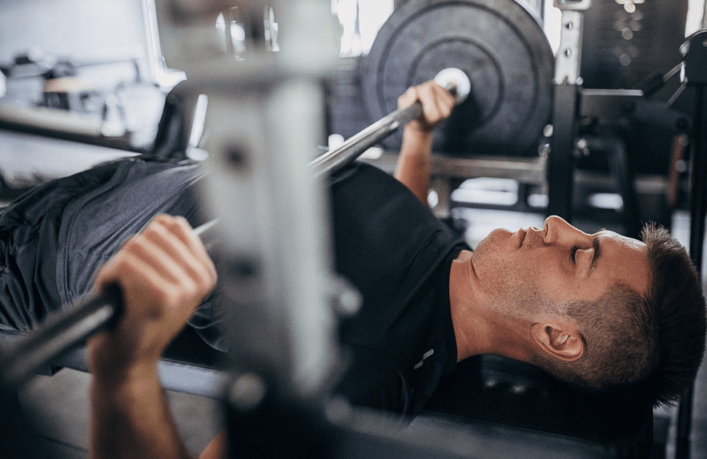 A black-haired man performs bench press in a gym