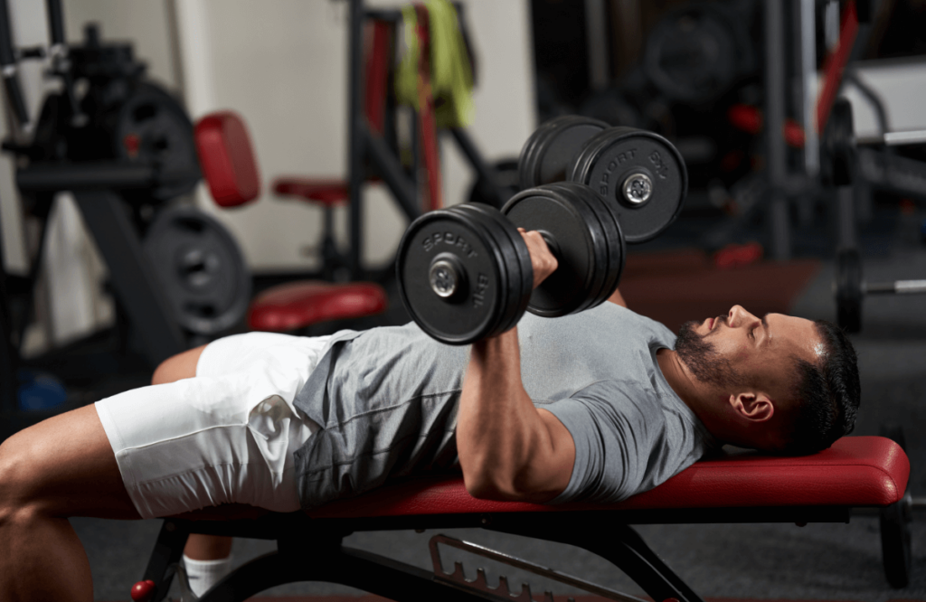 Fit man does bench dumbell press in a gym