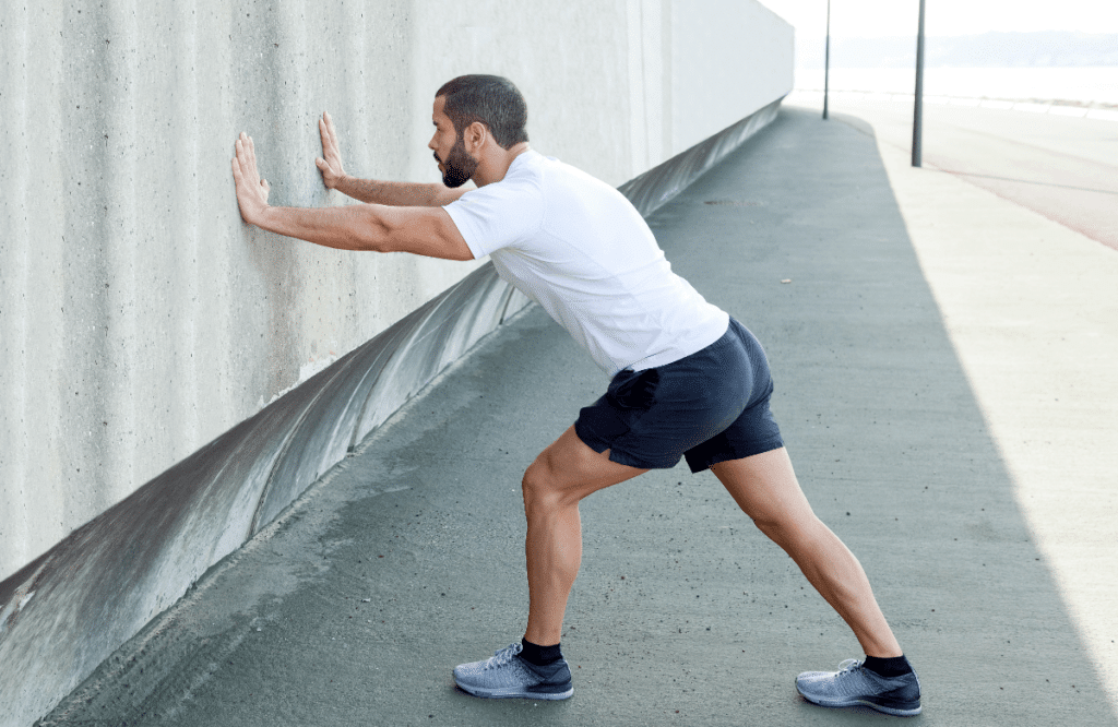 A man stretches his calves against a wall