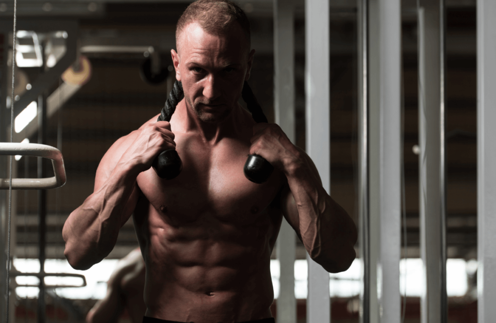 Muscular shirtless man grabs rope pulley in a gym