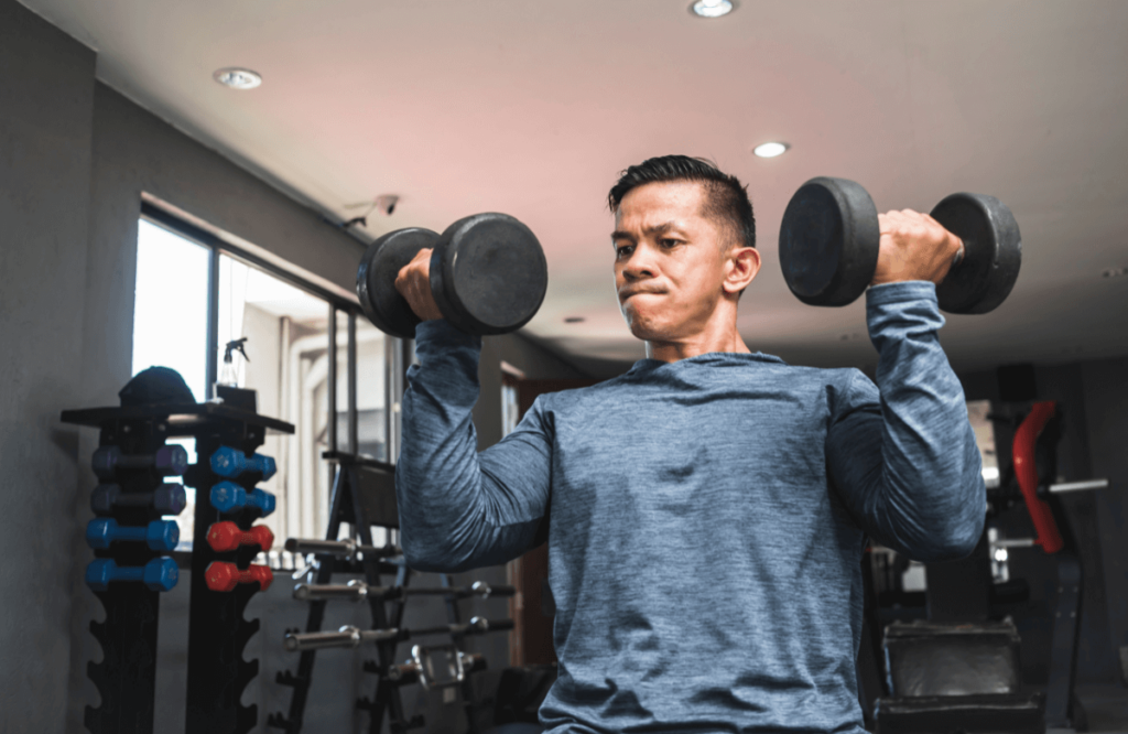 A man does arnold presses in a gym