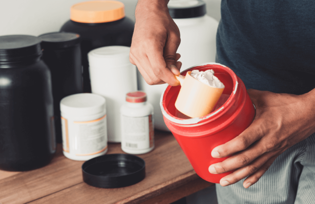 A man withdraws a scoop of creatine powder from its box