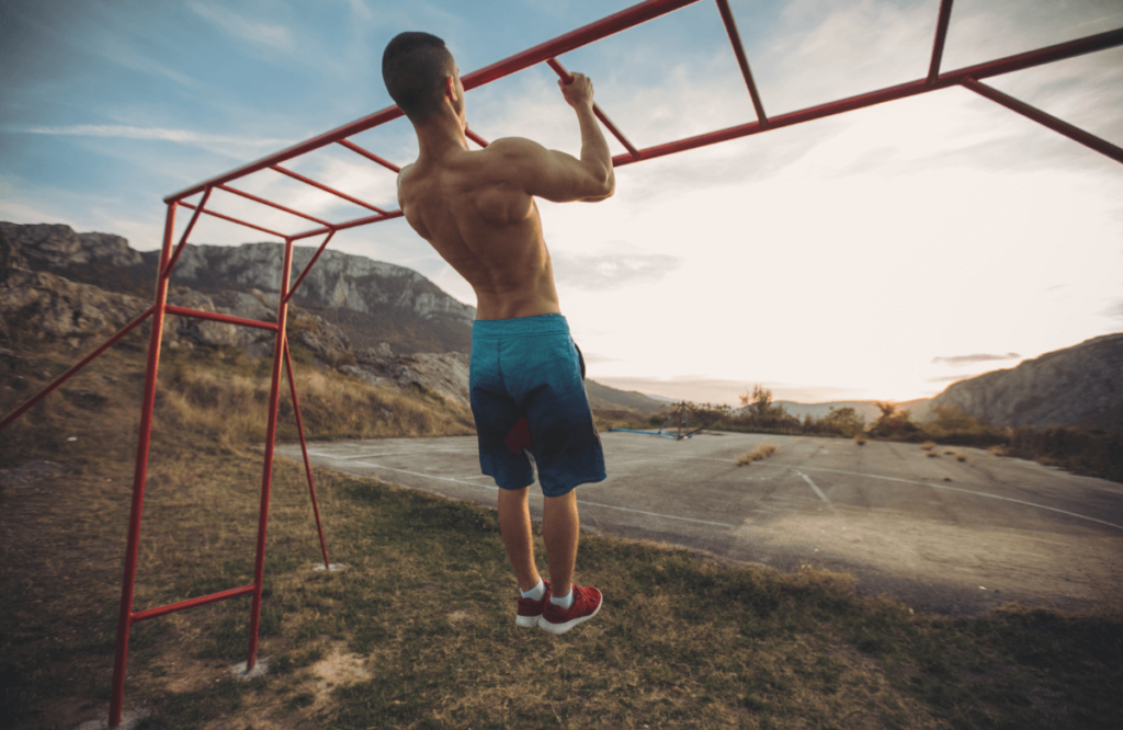 Shirtless man does neutral grip pull ups outside