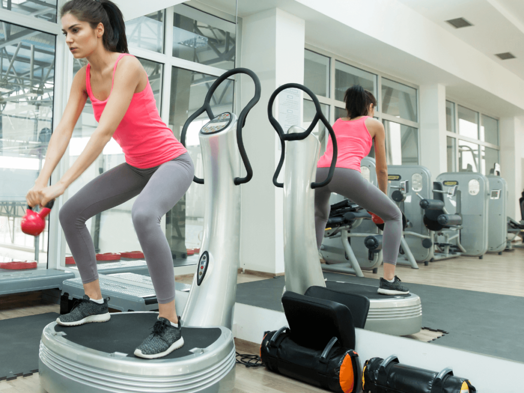 A woman trains on vibration plate with a kettlebell