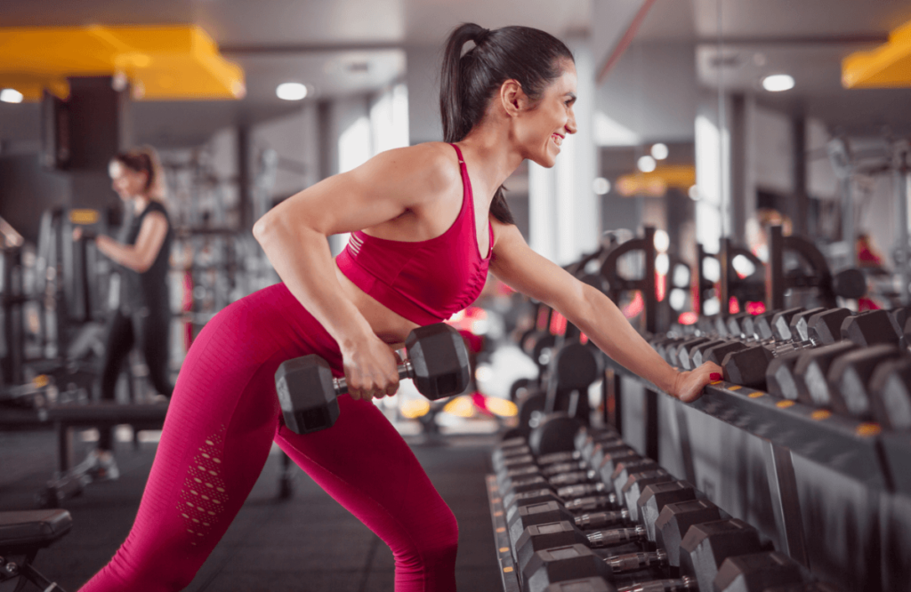 A smiling woman does dumbbell rows in a gym