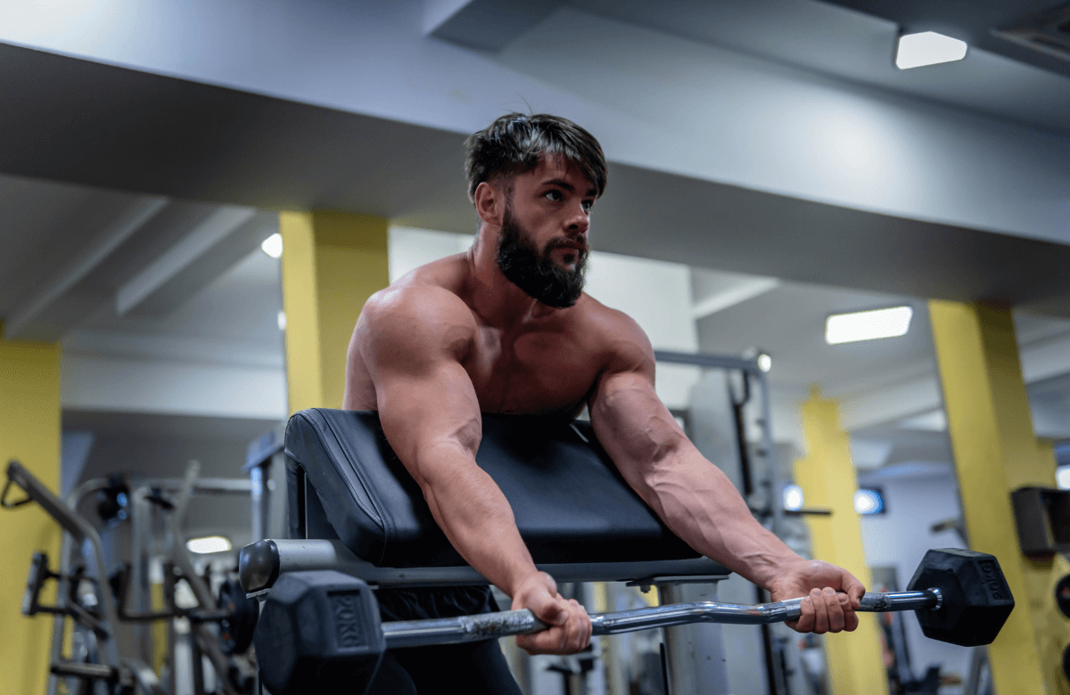 A muscular guy doing spider curls at the gym