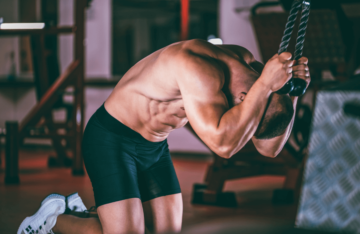 A muscular man does cable crunches in a gym