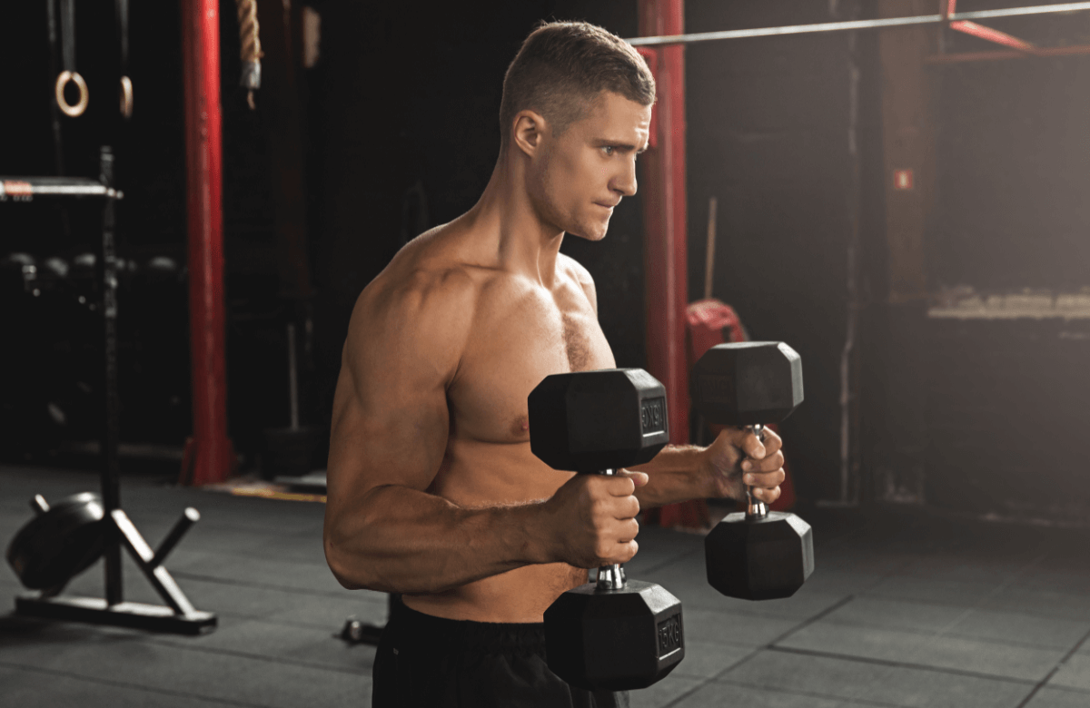 A shirtless muscular man does a dumbbell bicep workout
