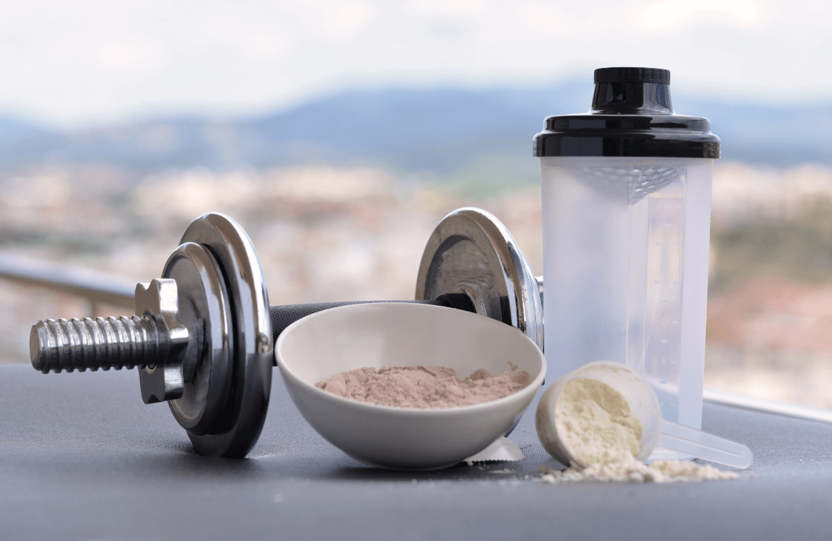 A scoop of protein powder, a dumbbell and a shaker
